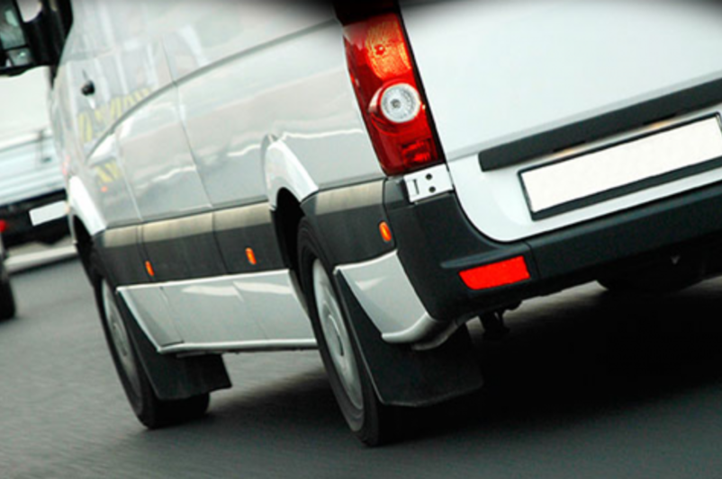 Ausschnitt von einem weißen Transporter, der einer Straße zwischen anderen Fahrzeugen fährt.